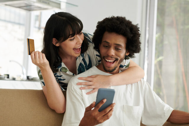 Happy young woman with credit card embracing her husband with smartphone.