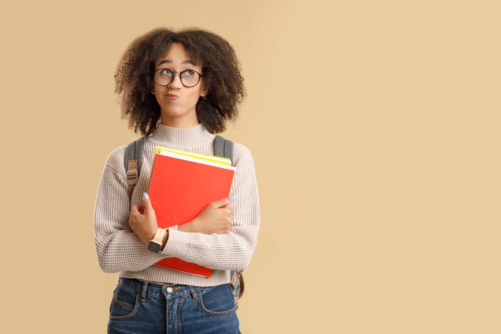 Young woman with afro wearing book bag holds textbooks and looks thoughtfully to the side.