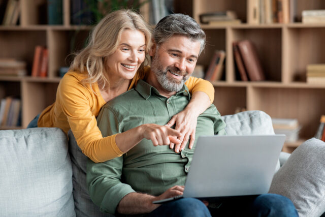 Middle aged couple browsing on laptop together on couch.