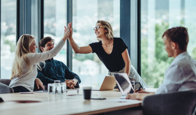 Group of work colleagues reach over conference table to high five.