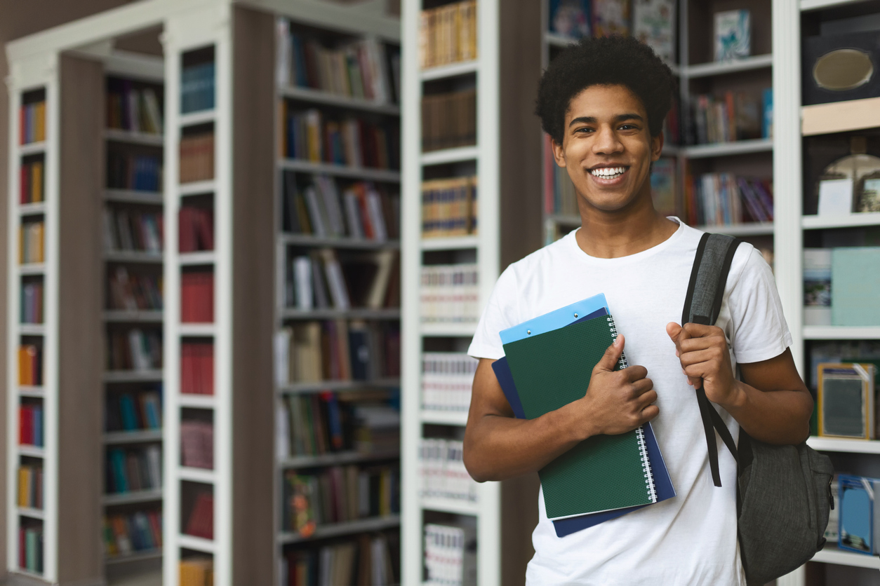 African American college student smiles while standing in university library.