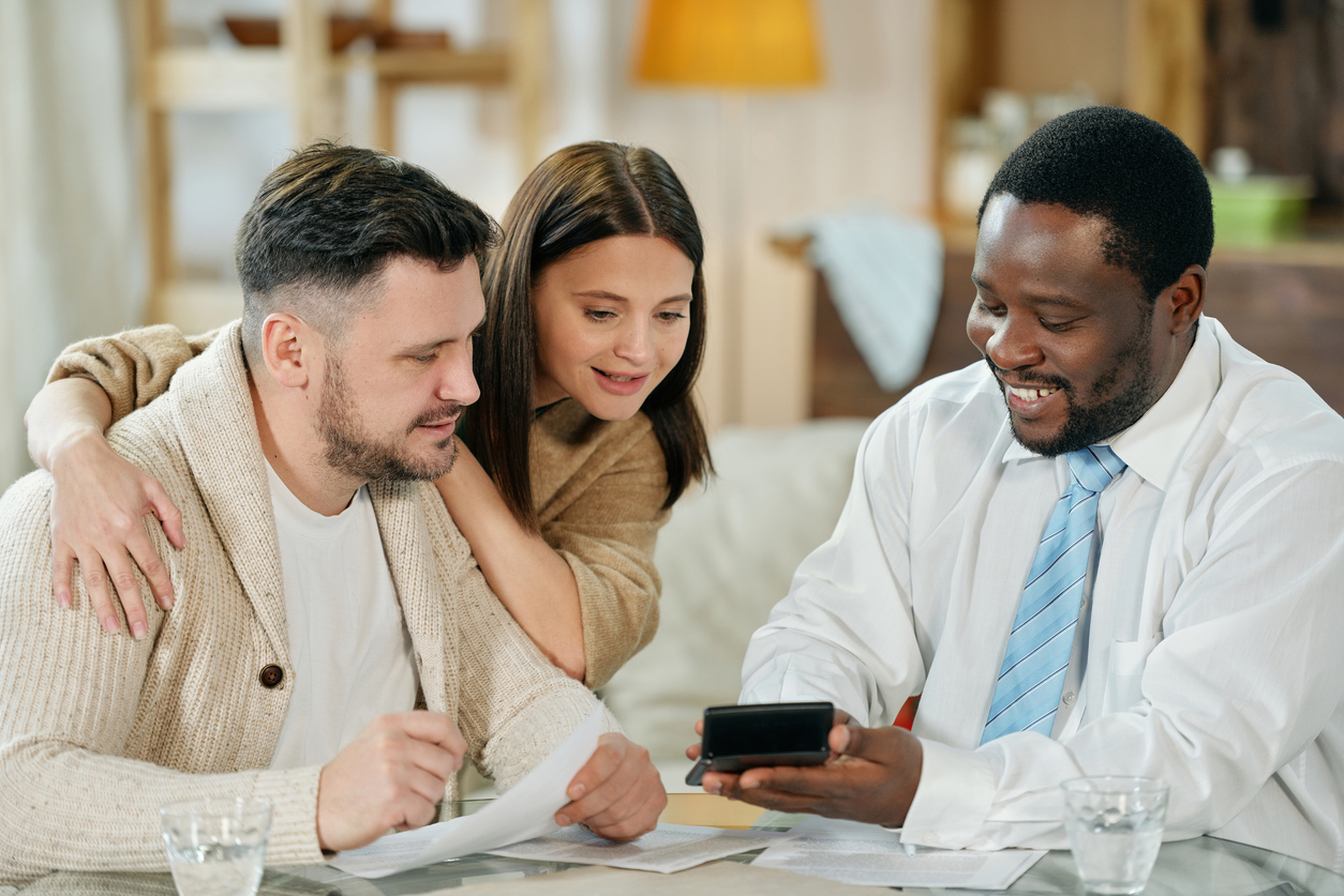 Adult smiling black man with calculating machine showing young couple their interest rate.