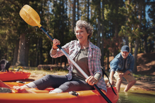 Portrait of happy senior woman paddling kayak in the lake with man supporting from behind.