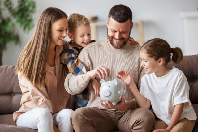 Happy family saves money together by putting a coin into a piggy bank.