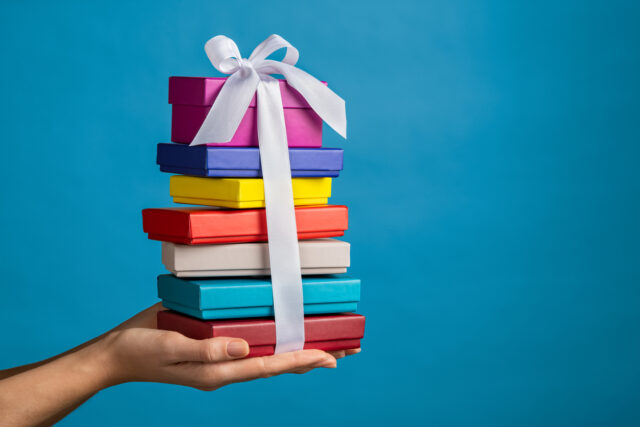 Hand holding pile of gift boxes with blue background.