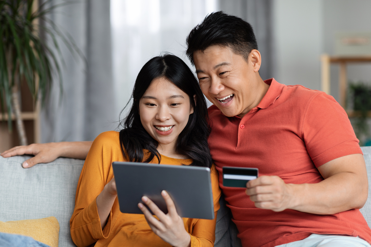Excited Asian husband and wife using tablet and credit card