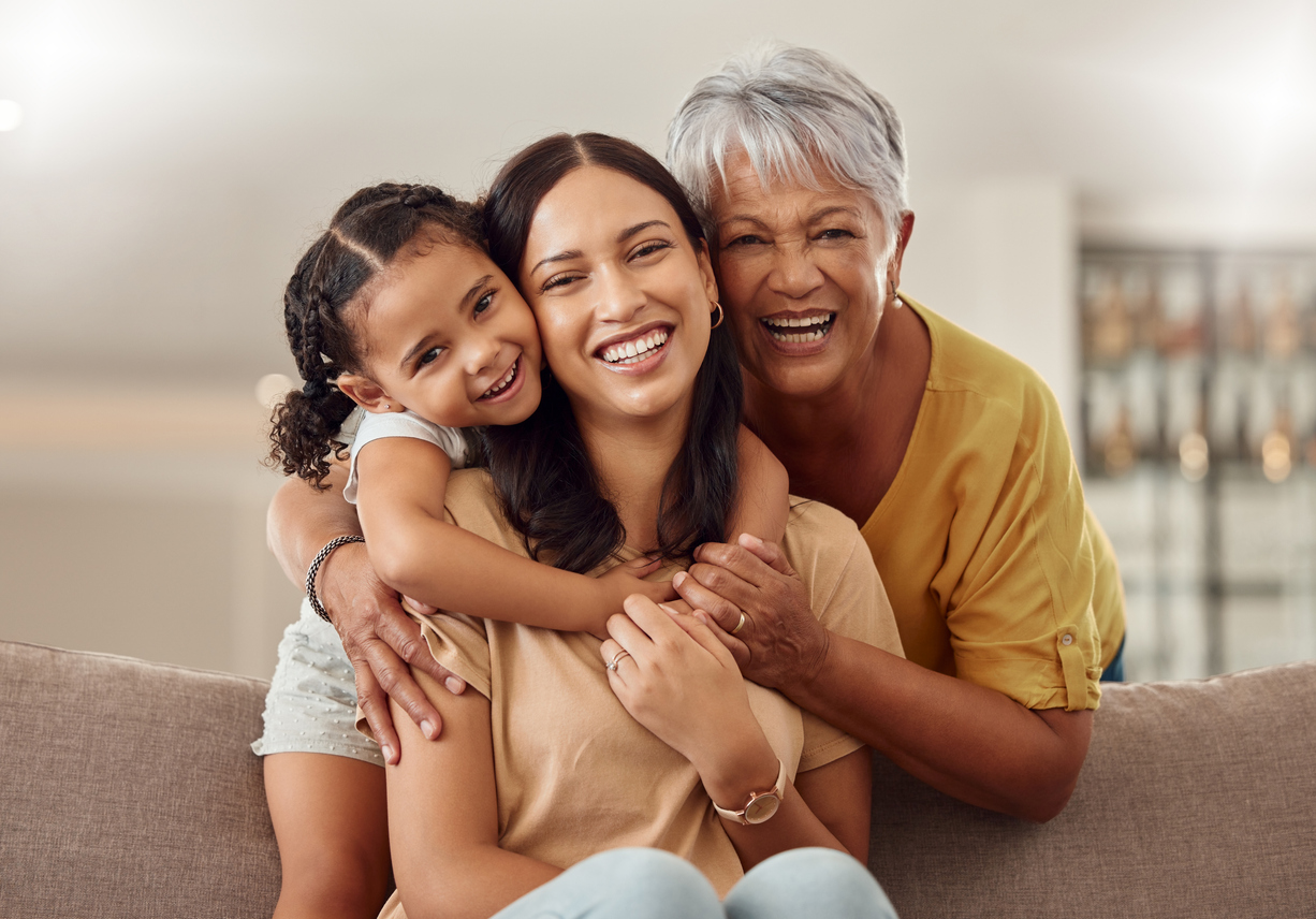 Grandmother, mother and child embrace happily on sofa.