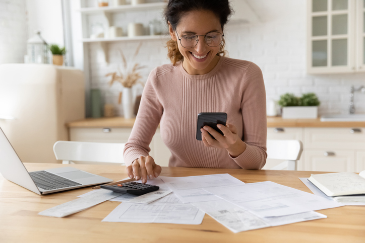 Smiling woman calculates payment costs on table with documents spread out. 