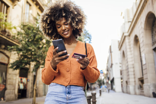 Happy African American woman with afro smiles at phone with credit card in hand.