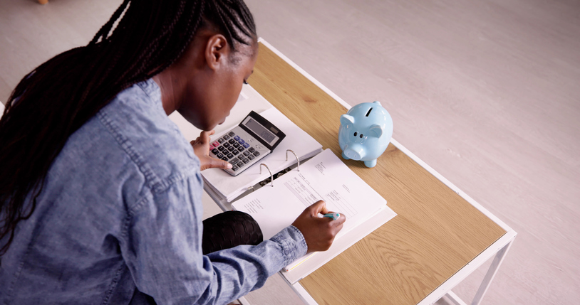 Young woman uses calculate to calculate budget with her savings in a piggy bank. 