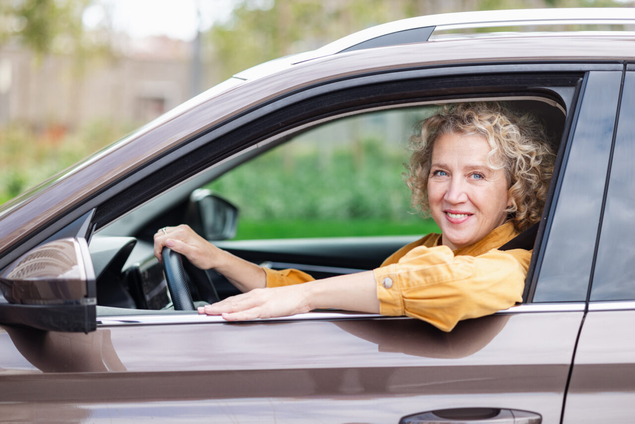 Older white woman stares contentedly from the driver's seat of her car.