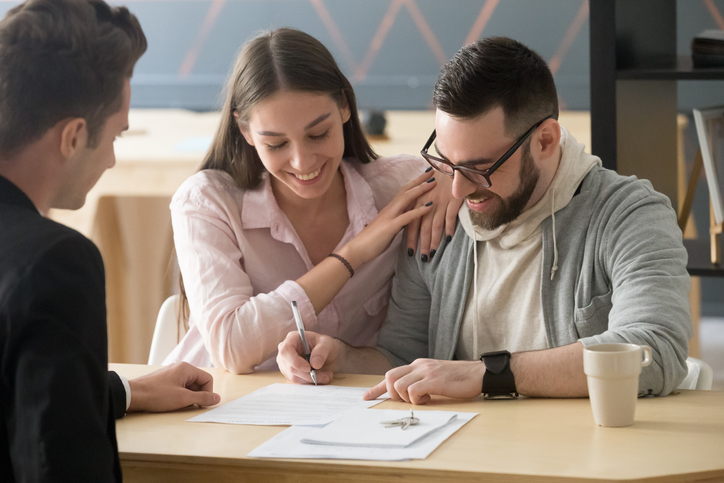 Young couple closes on house by signing official document with financial counselor. 